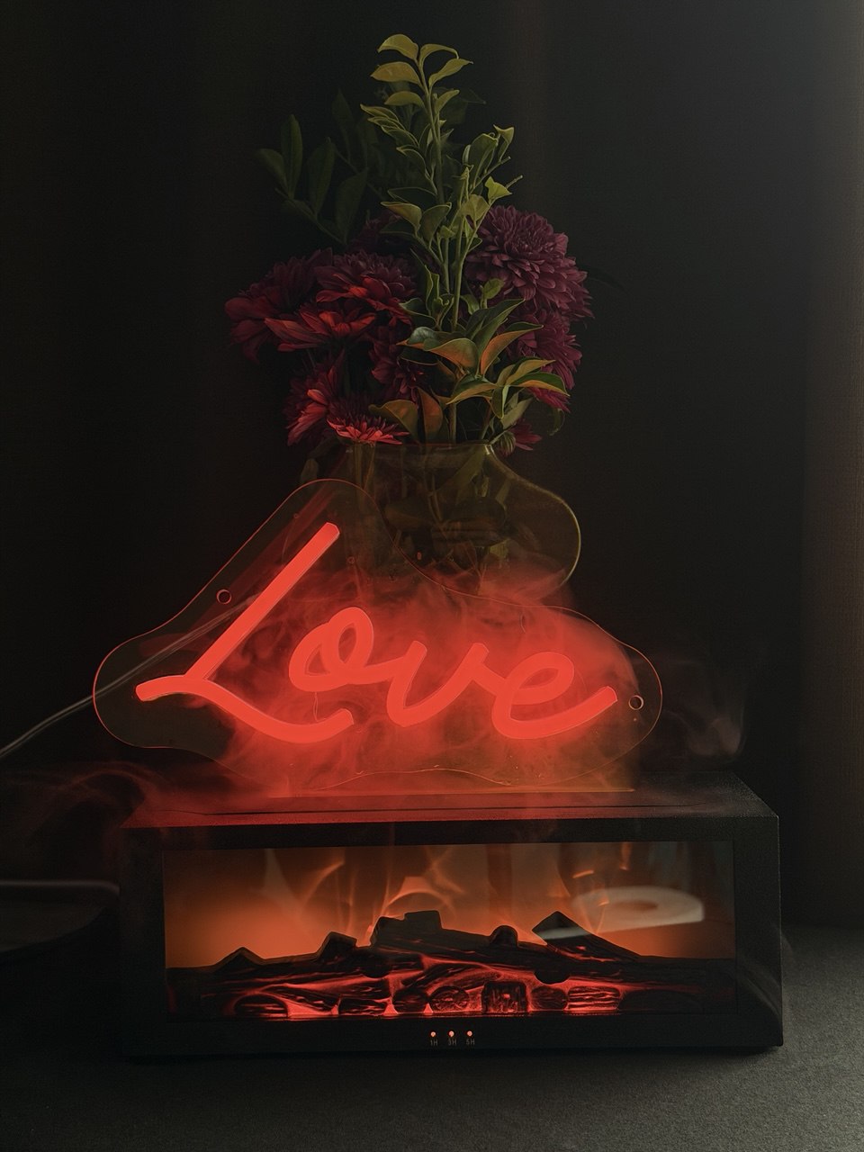 Decorative lamp with 'Love' neon sign and floral arrangement in a dark setting